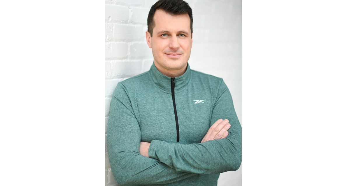 Man in green zip up stands with arms crossed against a wall