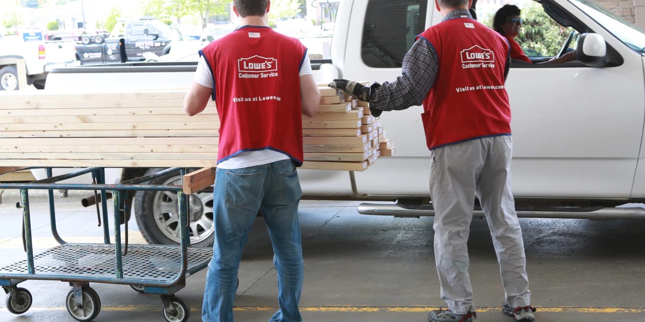 Workers in red Lowe's branded vests pile plywood into white truck