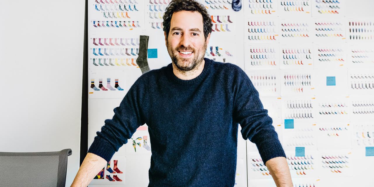 Bombas co-founder Randy Goldberg stands in front of a wall with prototypes of socks