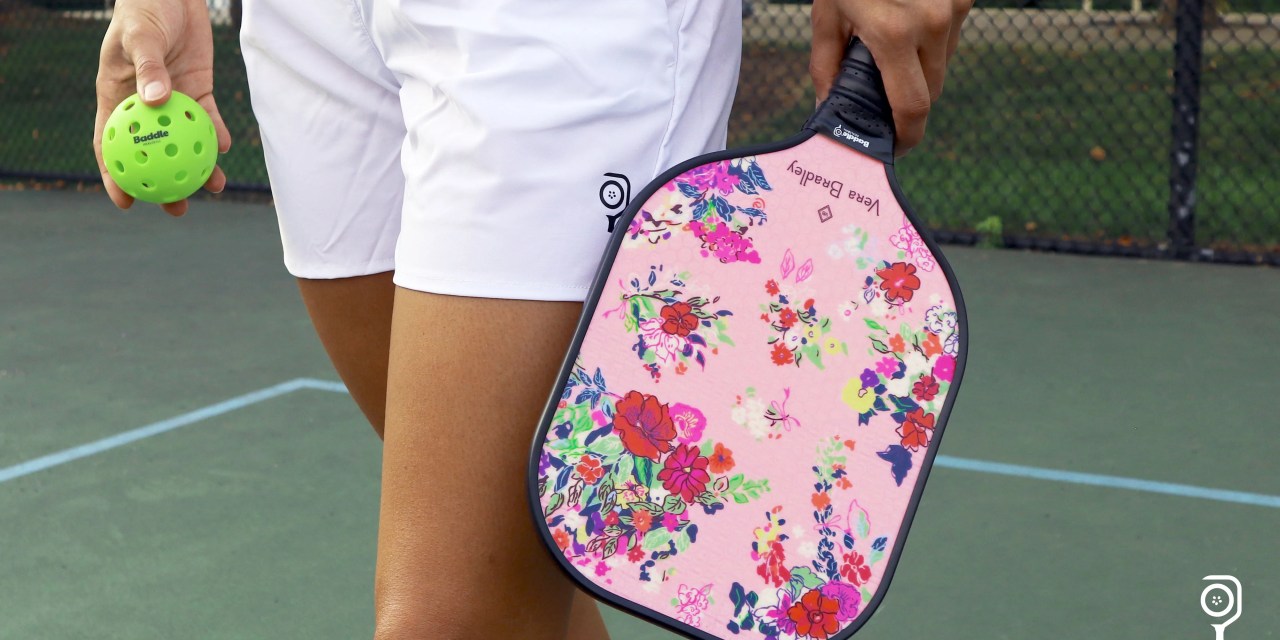 Model in white shorts holding a pickleball and a Vera Bradley paddle