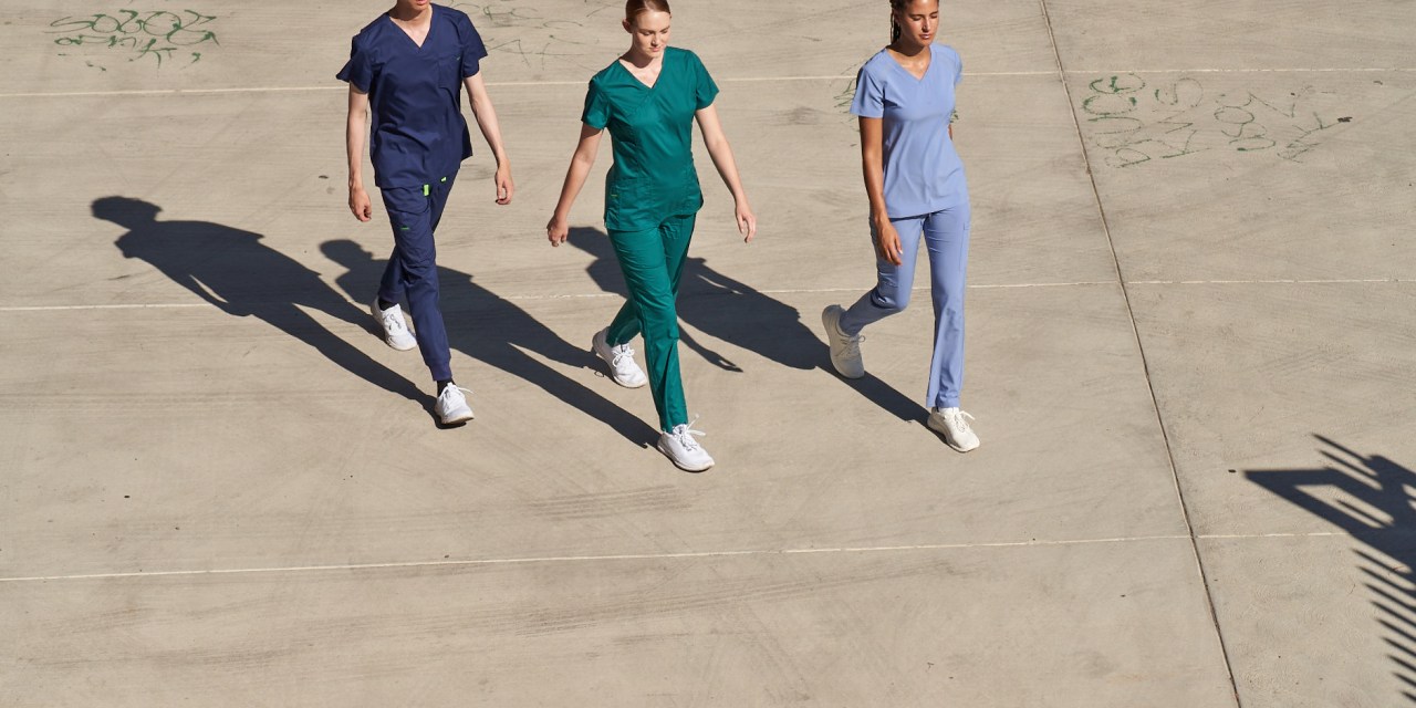 Three people in scrubs from Kindthread walk across a parking lot