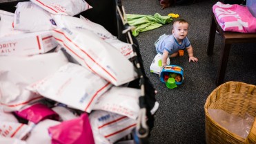 A baby crawling on the floor next to a bucket of mailers