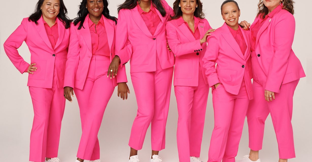A group of women wearing hot pink suits and white sneakers in a photo shoot.