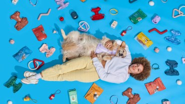 A woman and a golden retriever lies on the floor with several Wild One products.