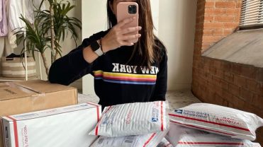 A woman takes a selfie with many postal packages around her.