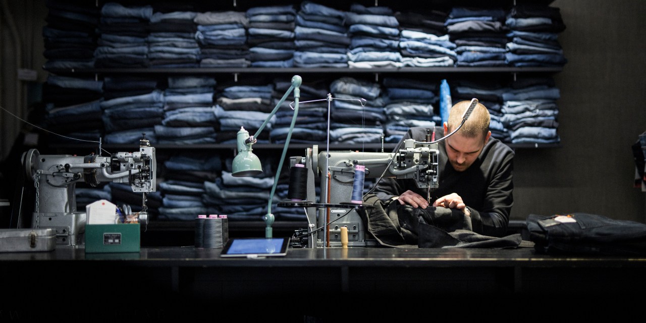 A man bends over a sewing table with a pair of denim jeans.