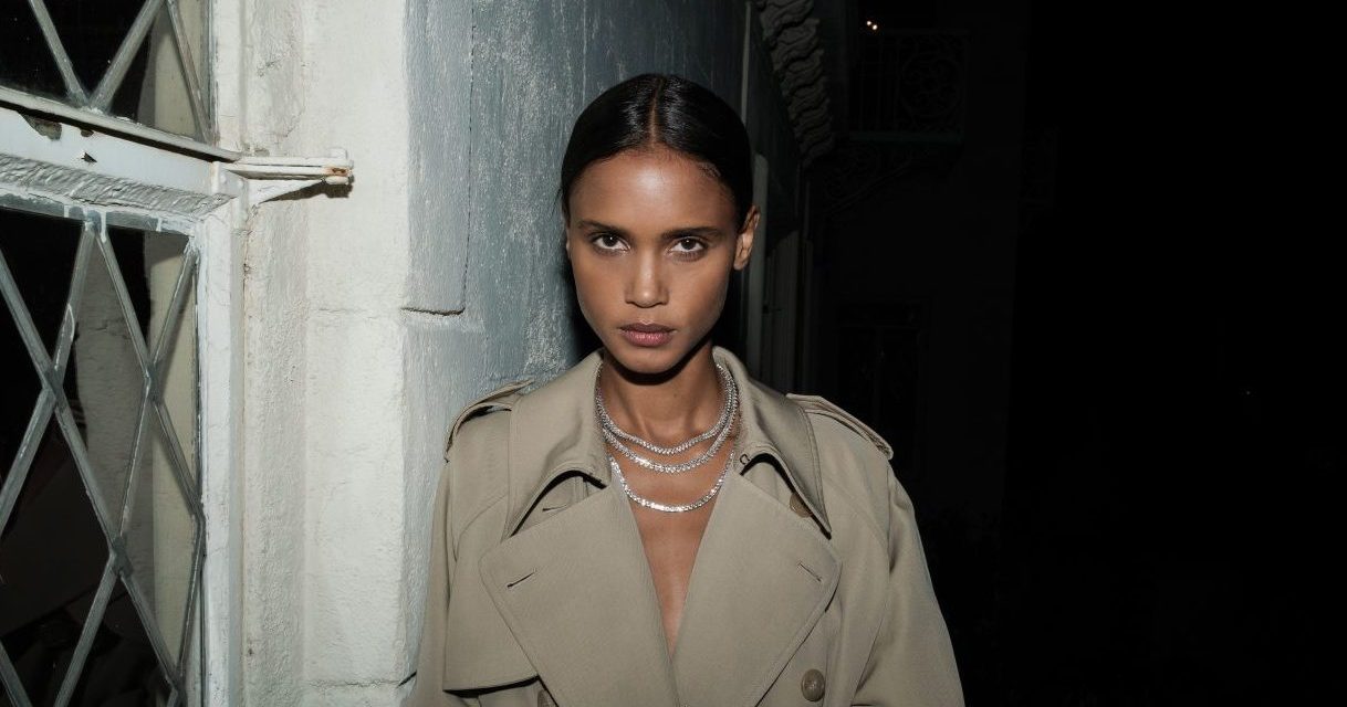 A model in a trench coat wears two white sapphire necklaces.