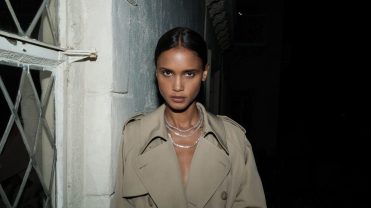 A model in a trench coat wears two white sapphire necklaces.