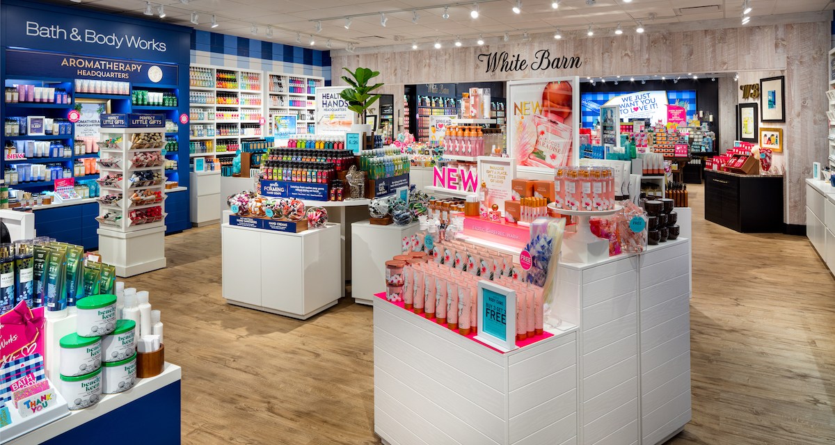 A Bath & Body Works store split into two sections; a Bath & Body Works section and a White Barn section, with displays featuring candles, soaps and other scented goods.