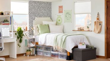 A twin bed with white bedding above containers in small dorm room.