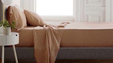 A bed with terra cotta sheets in front of a sunny window